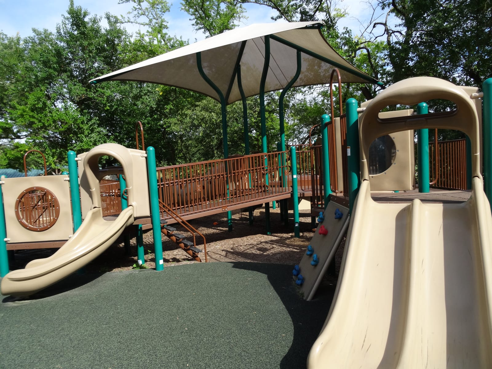 Wide view of the Can-Do Playground at Alapocas Run State Park, with colorful accessible play structures under mature trees