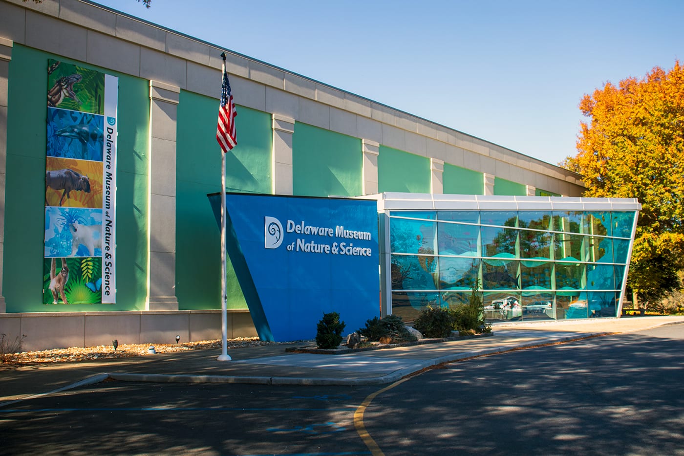 The Delaware Museum of Nature & Science entrance on Kennett Pike, with its blue sign and glass atrium, on a sunny fall day