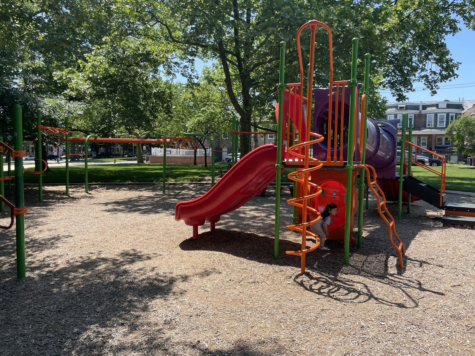 The playground beside Woodlawn Library, with a red slide and shade trees
